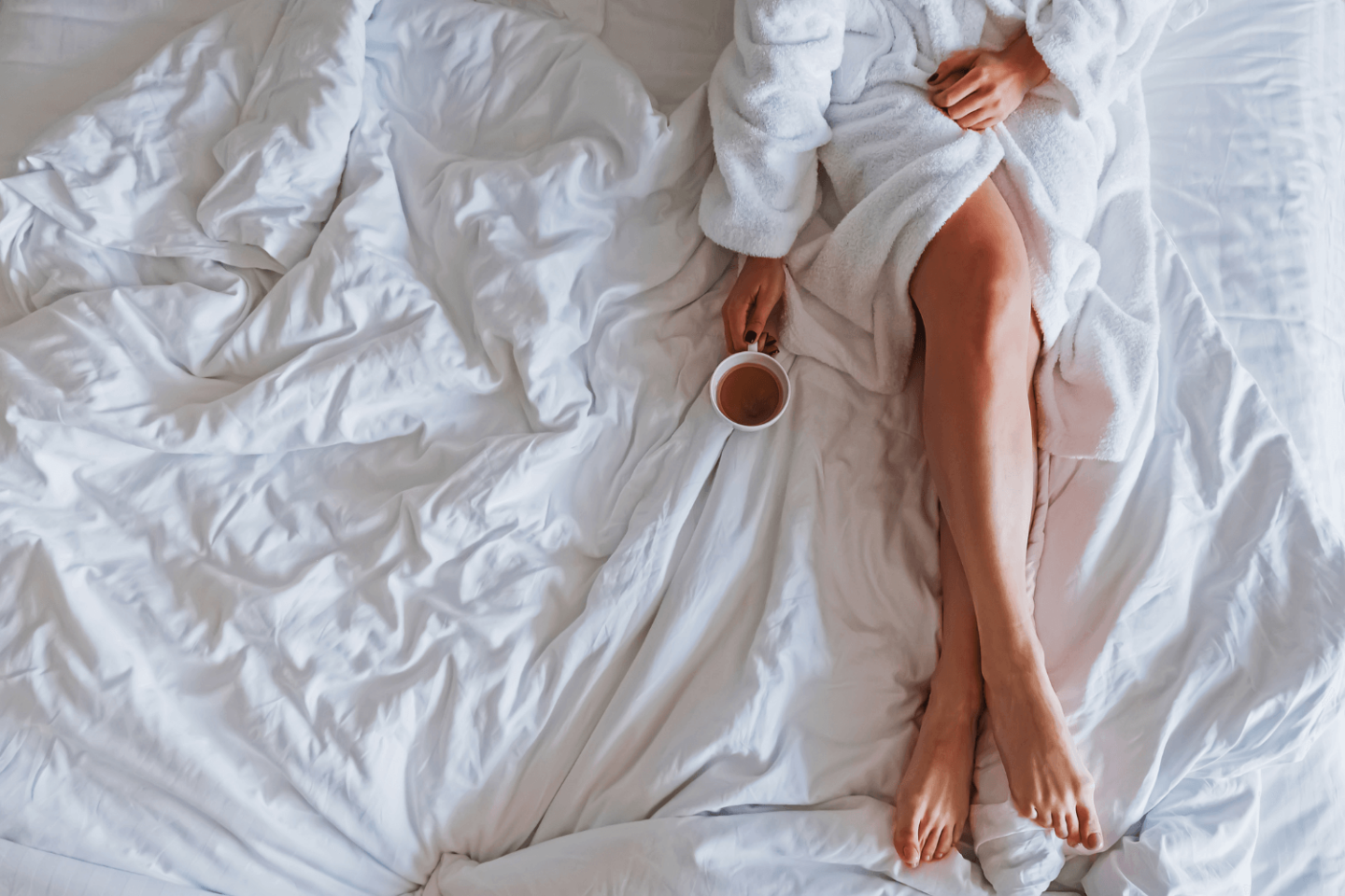 Woman holding mug of coffee in bed, about to start her productive morning routine.