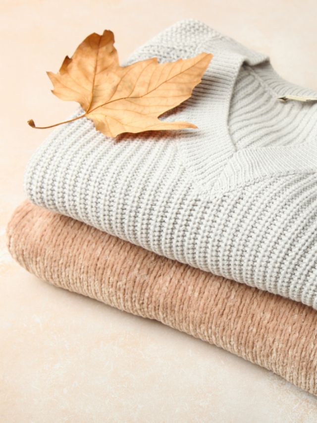 Two neutral coloured folded sweaters with an autumn leaf on top - sweaters are an essential part of an autumn capsule wardrobe