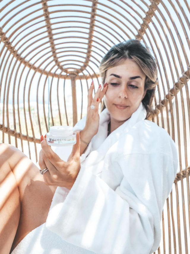 Woman on a bamboo chair while applying facial skin care after being inspired by skin care quotes.