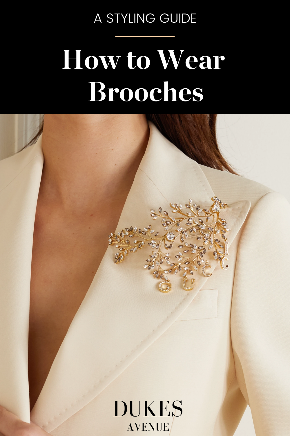A woman wearing a big gold brooch with diamonds on a light pink blazer with text overlay "A styling guide - how to wear brooches"