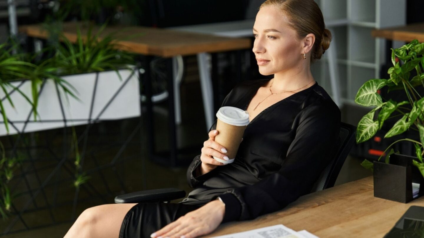 A young plus size woman relaxes at her desk drinking coffee while working on her assignments.