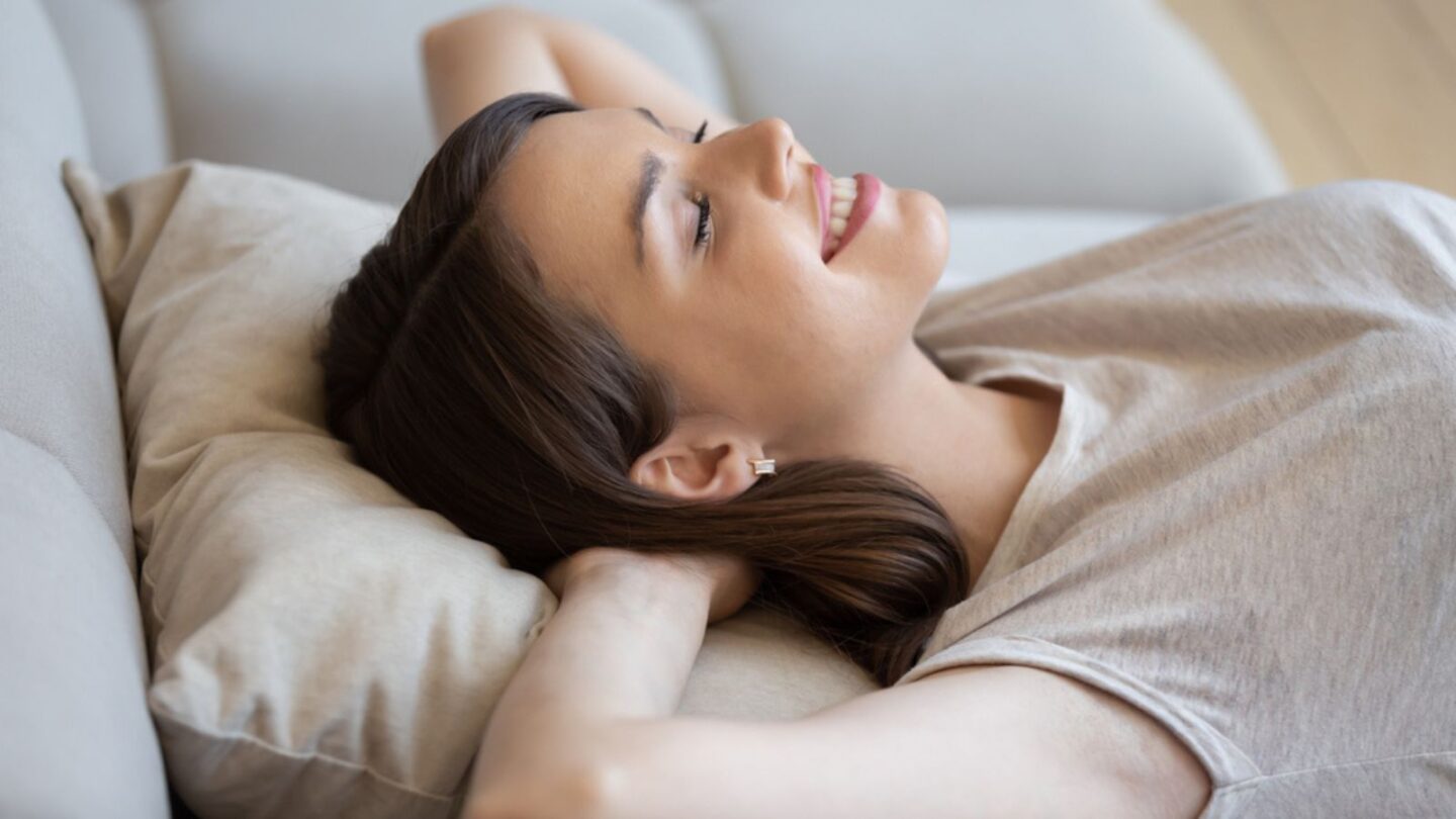 Happy relaxed woman lying on couch with eyes closed and enjoying peace and quiet of her own soundproof house