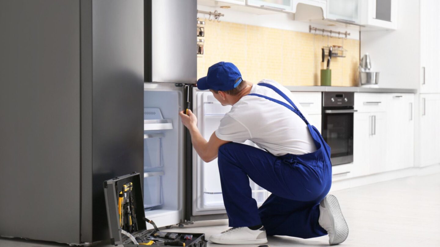 Male technician with screwdriver repairing refrigerator in kitchen