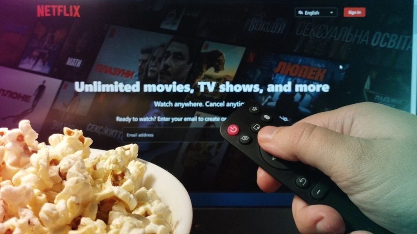 Person watching Netflix on TV with popcorn and remote control