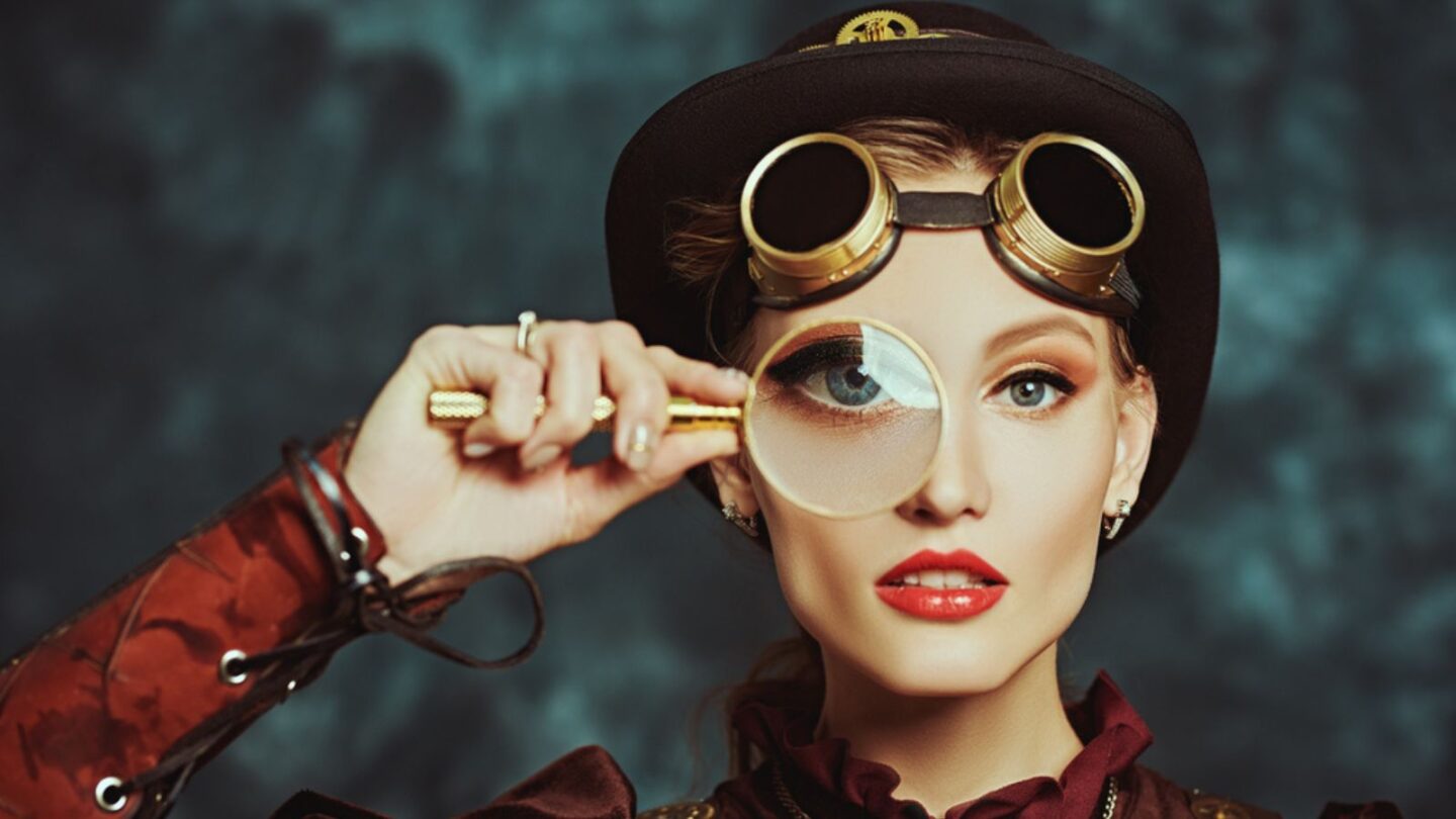 Portrait of a beautiful steampunk girl with a magnifying glass on a grunge background