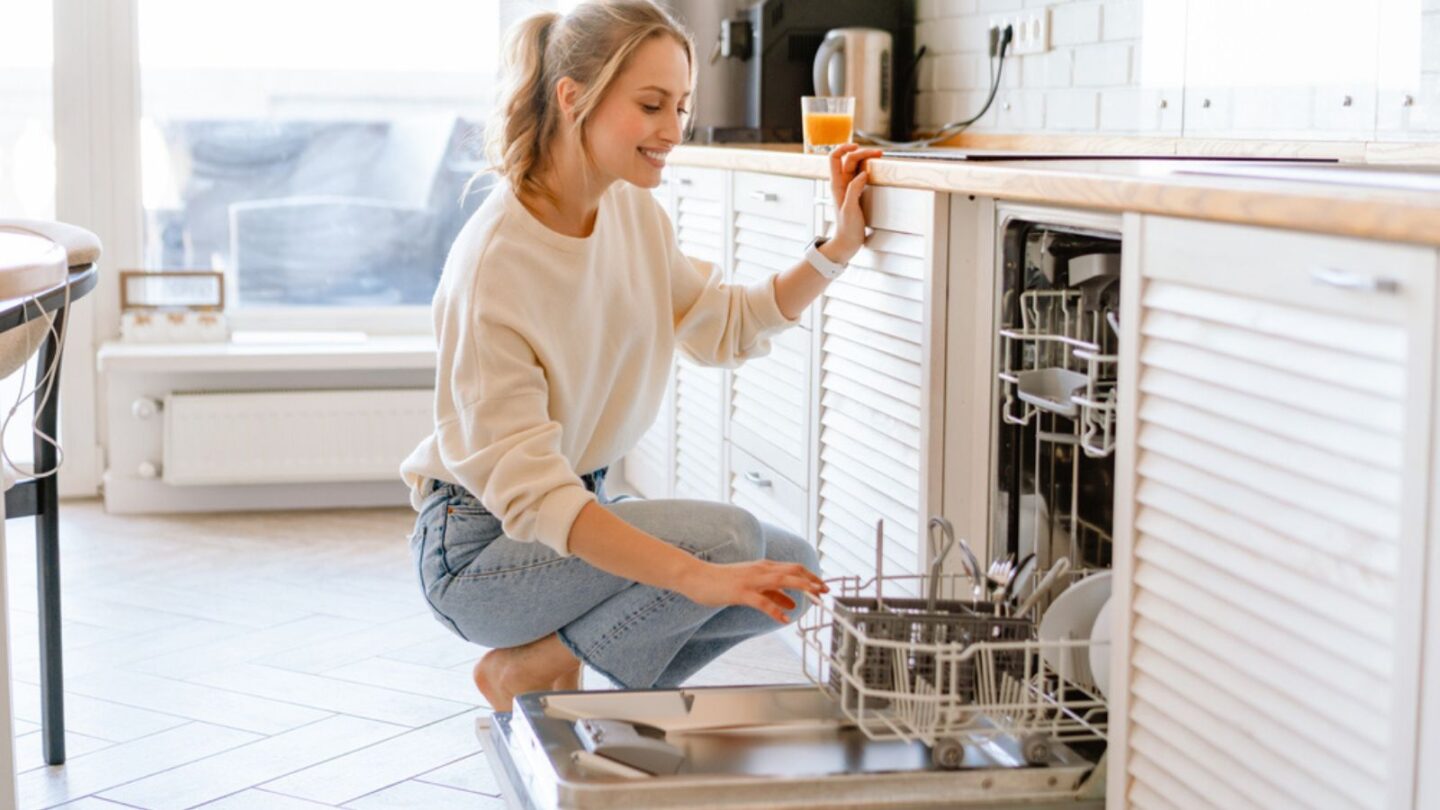 Smiling young white woman putting dishes in the dishwasher at home