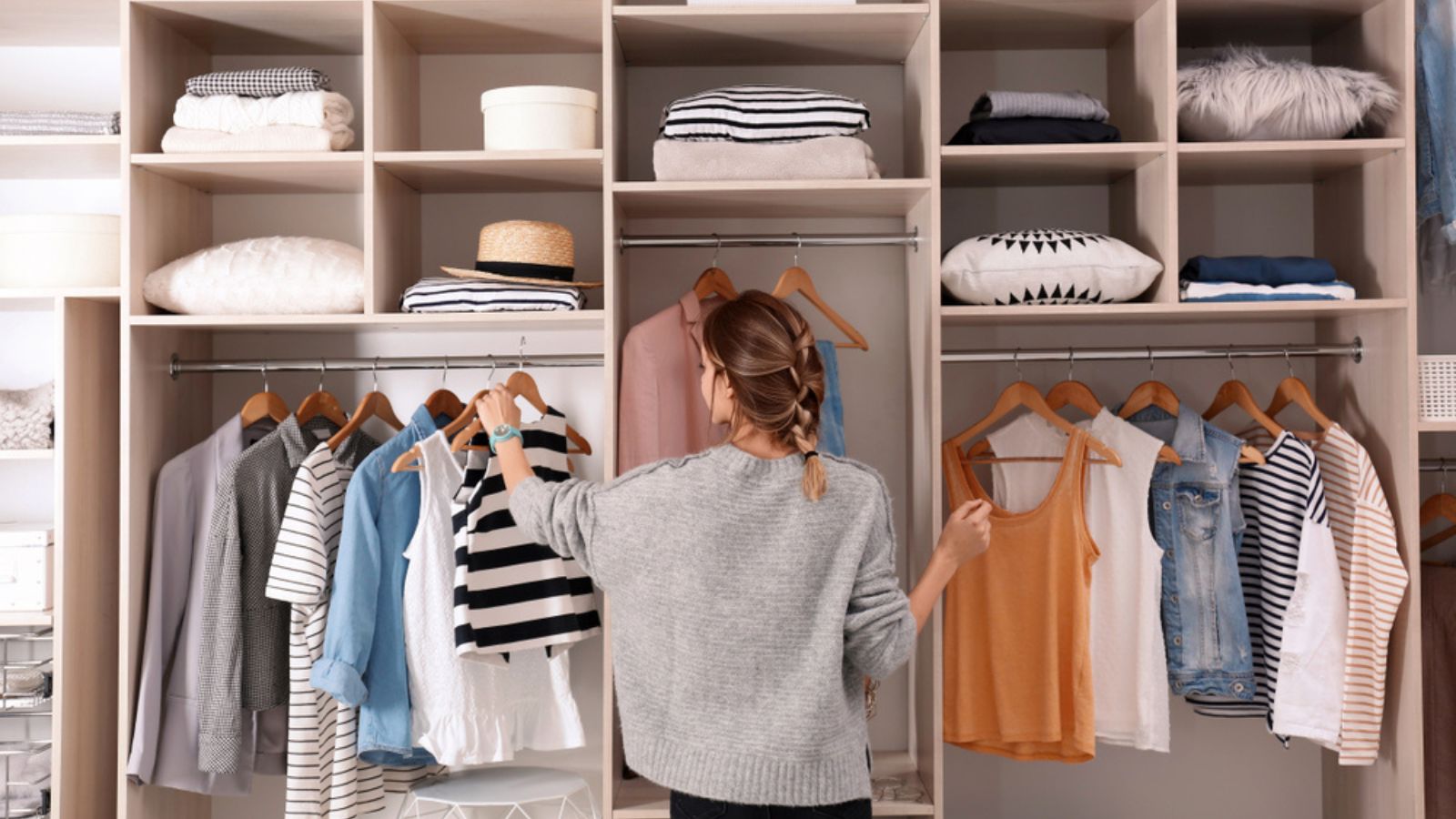 Woman choosing clothes from large wardrobe closet with stylish clothes and home things