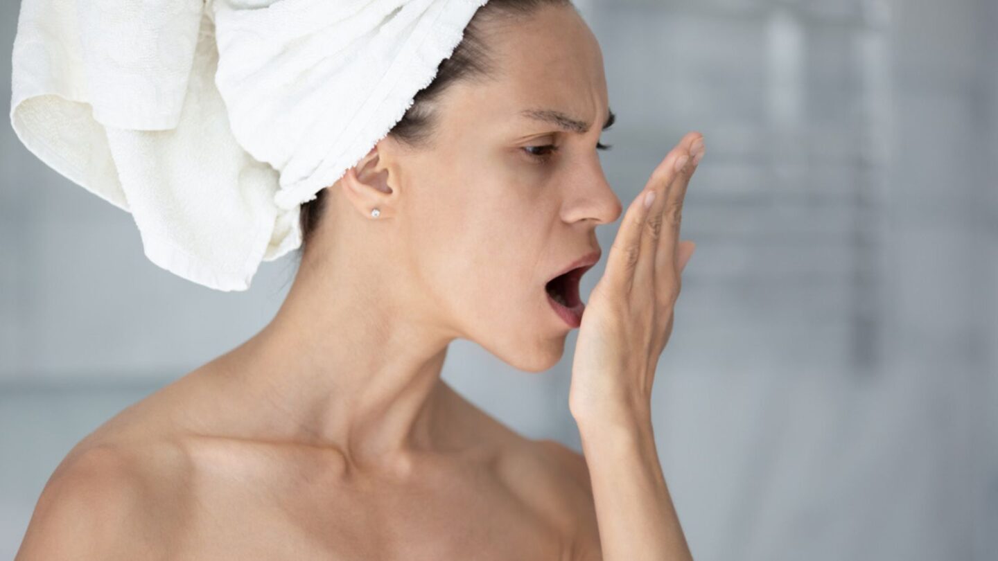 Woman with towel on head put palm in front face opens mouth check breath close up image