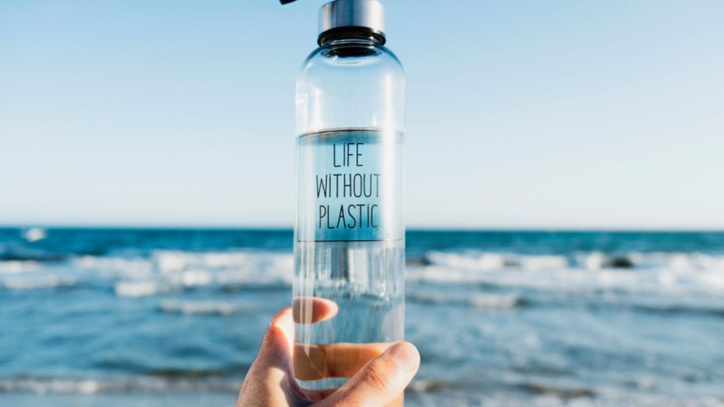 caucasian man holding a glass reusable water bottle with the text life without plastic written in it