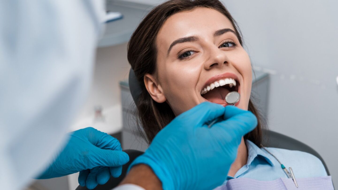 selective focus on dentist in latex gloves holding dental mirror near woman