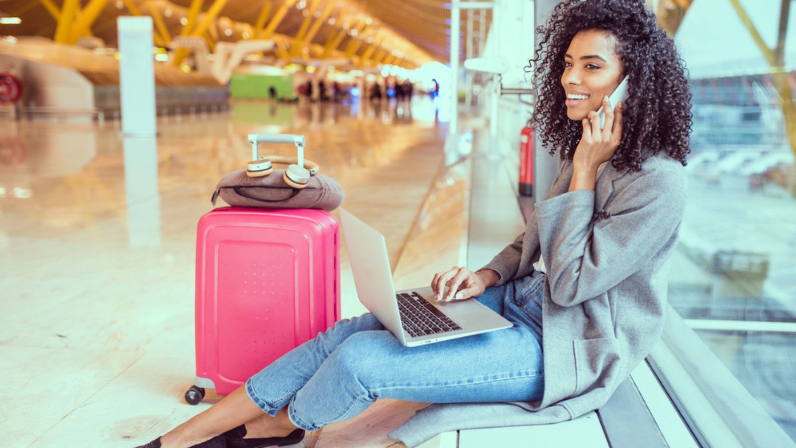 woman using mobile phone and laptop at the airport sitting by the window